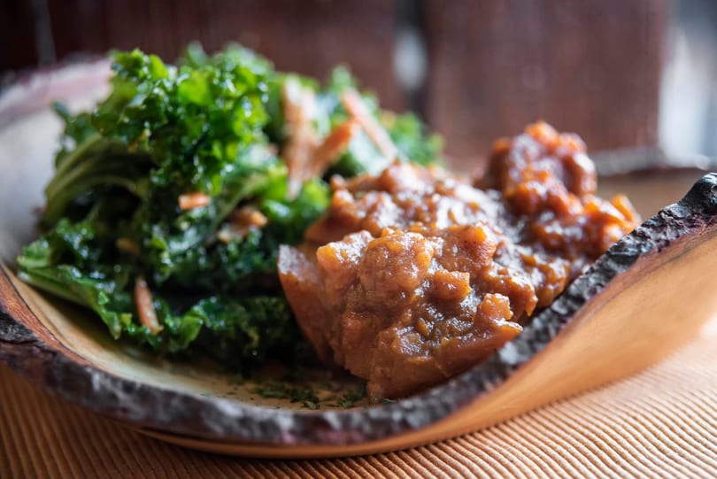 Close-up of a dish with green kale and a rich, brown stew on a rustic plate.