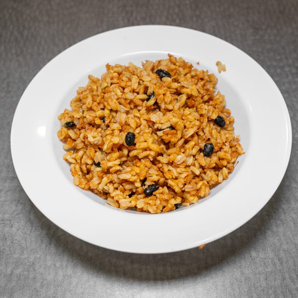 A white bowl filled with orange-brown rice and black beans, on a gray surface.