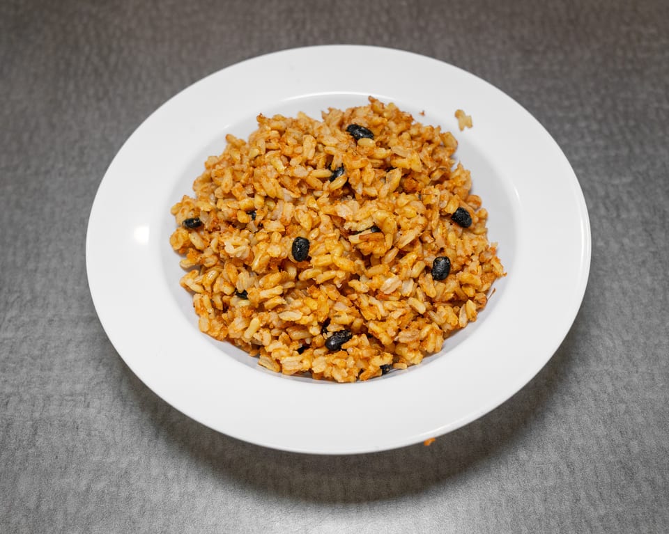 A white bowl filled with orange-brown rice and black beans, on a gray surface.