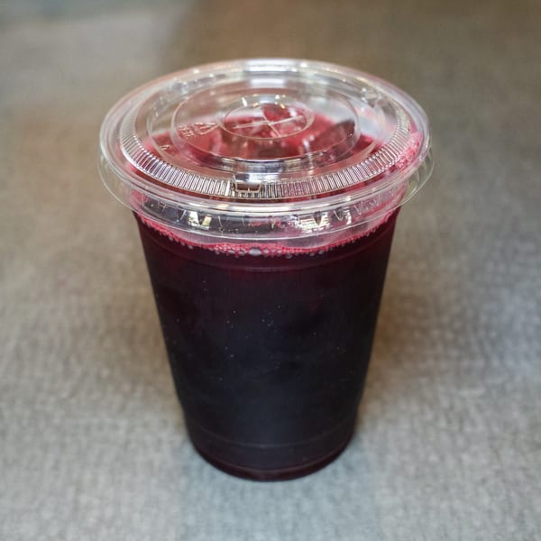 A clear plastic cup filled with a dark red beverage and topped with a clear lid.