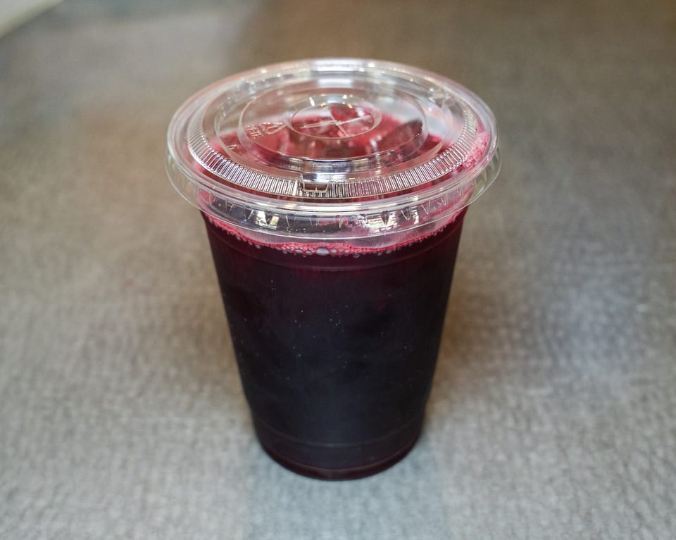 A clear plastic cup filled with a dark red beverage and topped with a clear lid.