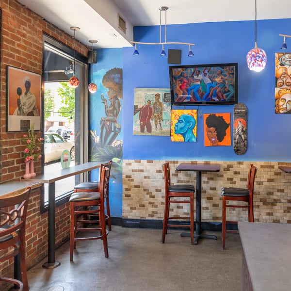Vibrant restaurant interior with blue walls, diverse artwork, bar seating, and small tables.