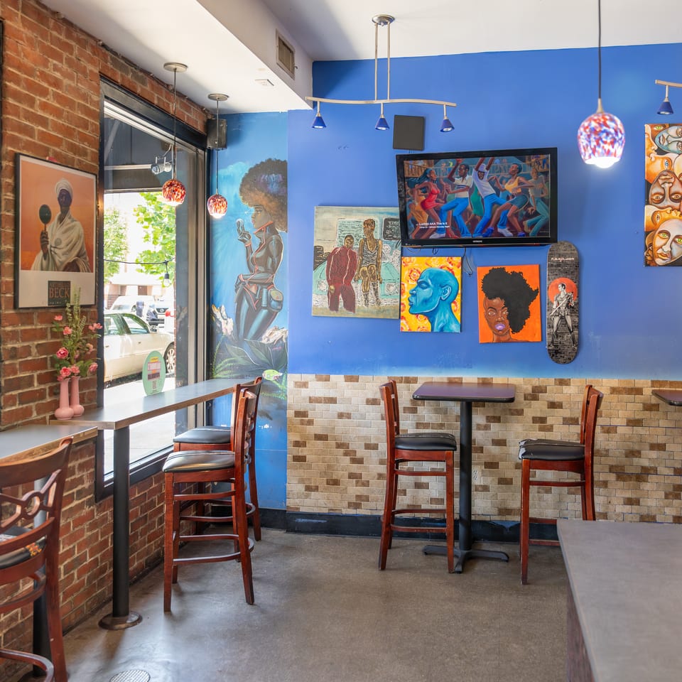 Vibrant restaurant interior with blue walls, diverse artwork, bar seating, and small tables.