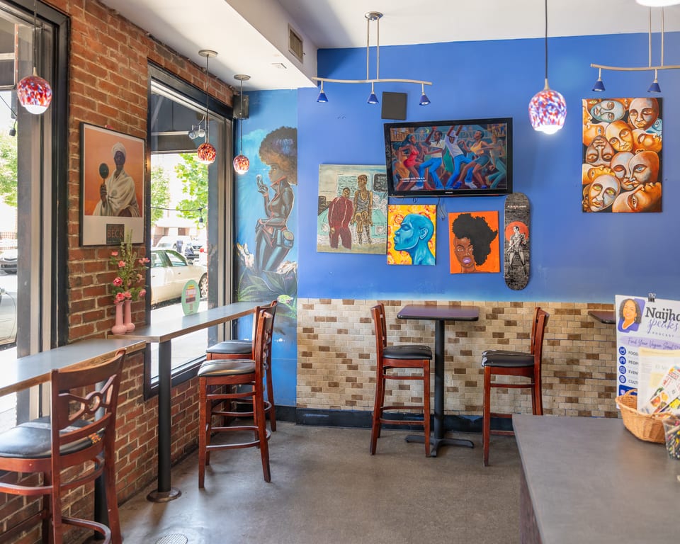 Vibrant restaurant interior with blue walls, diverse artwork, bar seating, and small tables.