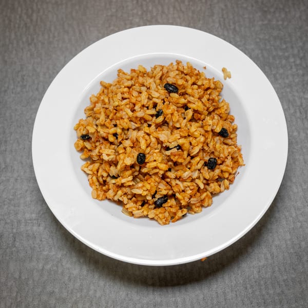 A white bowl filled with reddish-brown rice and black beans, centered on a gray surface.