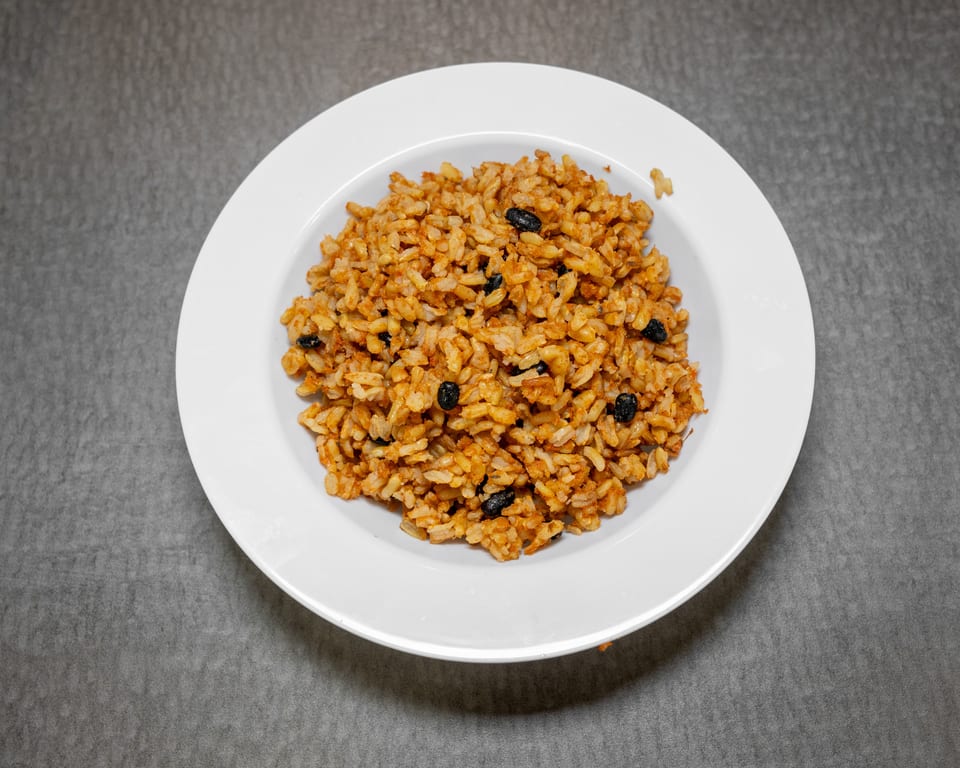A white bowl filled with reddish-brown rice and black beans, centered on a gray surface.
