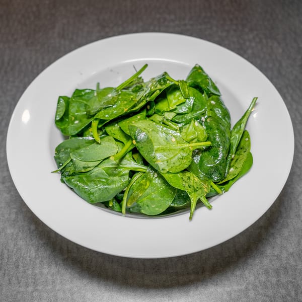 A white bowl filled with fresh, vibrant green spinach leaves, lightly dressed and seasoned.