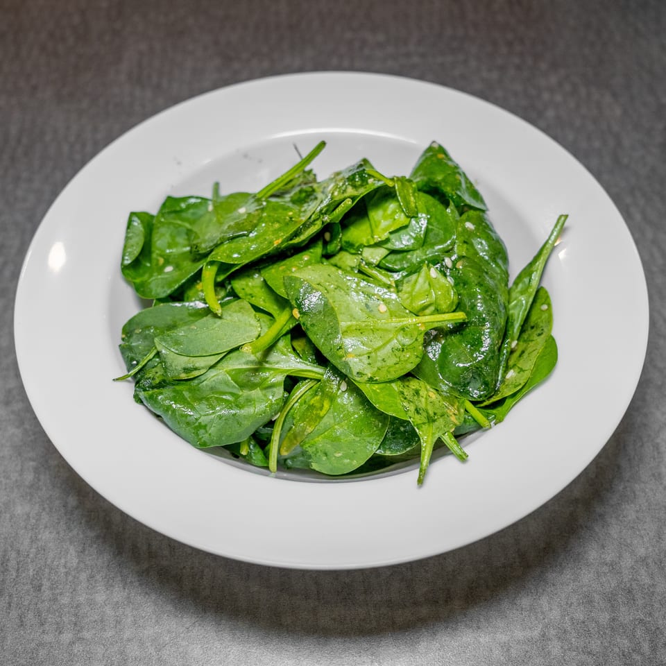 A white bowl filled with fresh, vibrant green spinach leaves, lightly dressed and seasoned.