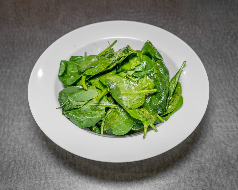A white bowl filled with fresh, vibrant green spinach leaves, lightly dressed and seasoned.