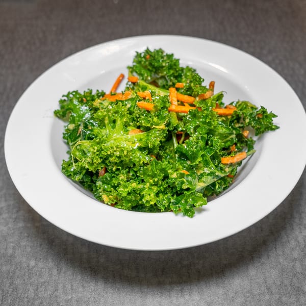 Vibrant green kale salad with shredded carrots and a creamy dressing in a white bowl.