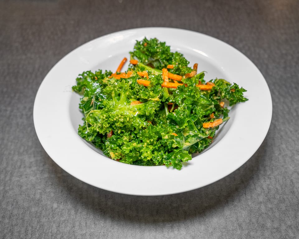Vibrant green kale salad with shredded carrots and a creamy dressing in a white bowl.