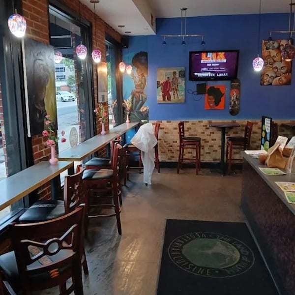 Interior of a restaurant with blue walls, window seating, high-top tables, and a counter.
