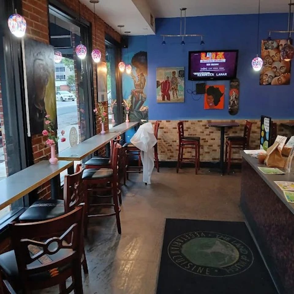 Interior of a restaurant with blue walls, window seating, high-top tables, and a counter.