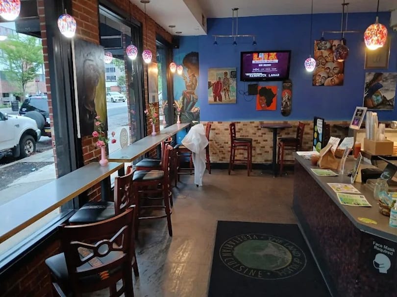 Interior of a restaurant with blue walls, window seating, high-top tables, and a counter.