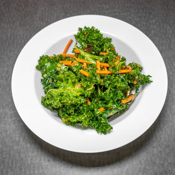 A white bowl filled with vibrant green kale and orange carrot strips, dressed with a light sauce.