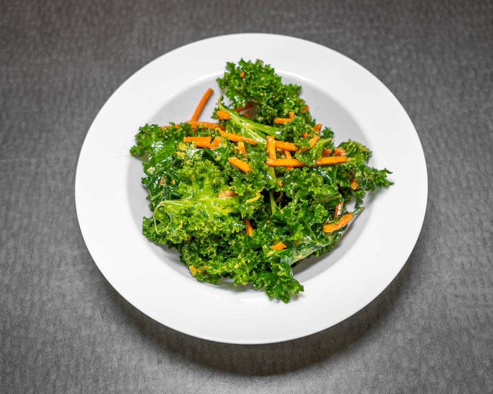 A white bowl filled with vibrant green kale and orange carrot strips, dressed with a light sauce.