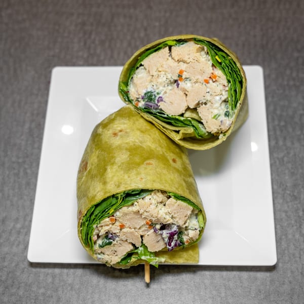 Two halves of a chicken salad wrap with spinach, carrots, and red cabbage on a white plate.