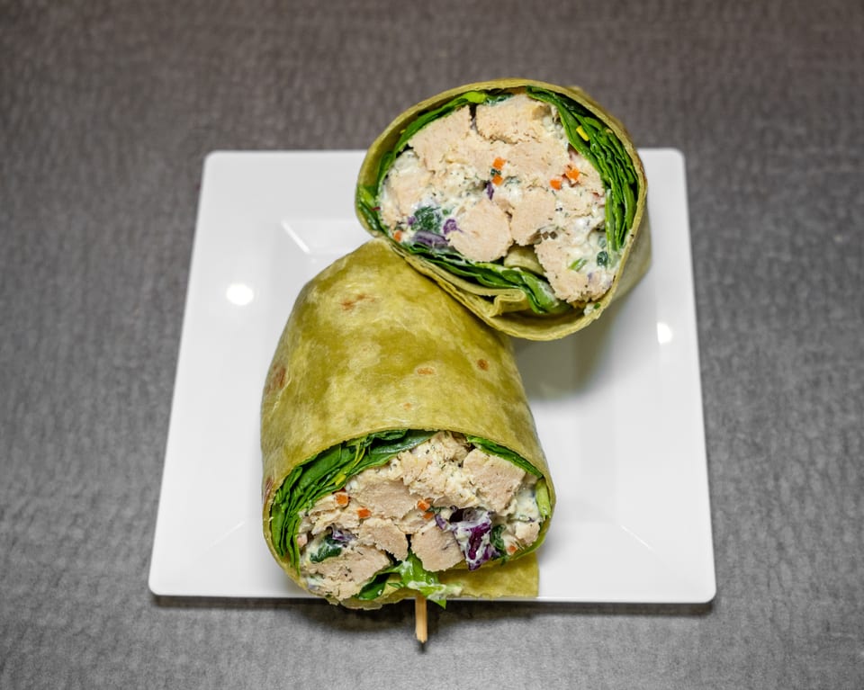 Two halves of a chicken salad wrap with spinach, carrots, and red cabbage on a white plate.