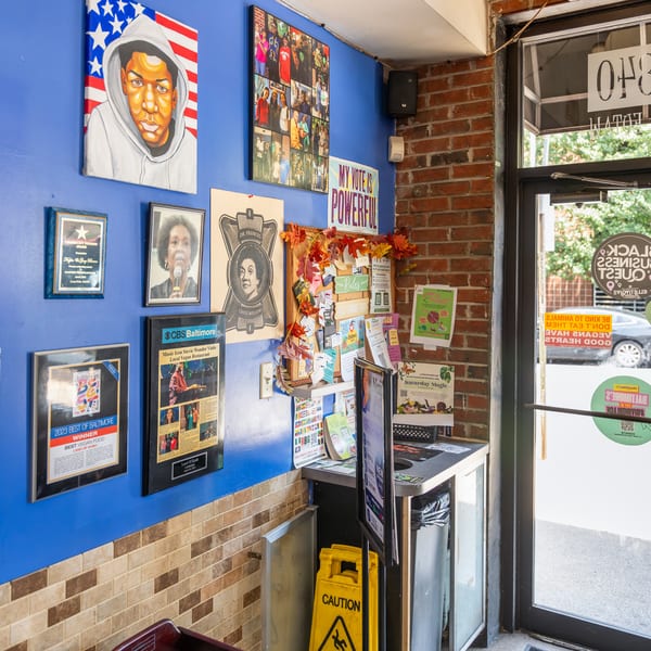 A vibrant blue wall adorned with diverse artwork and awards, next to a brick wall and glass door.